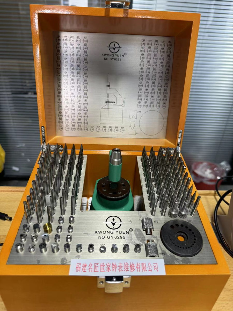 An open wooden case holding a complete watchmaker's tool set: screwdrivers, tweezers and a movement holder