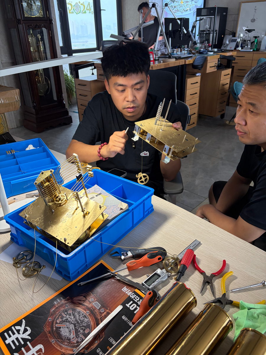 A student holding up a brass clock movement beside a tray of parts and hand tools